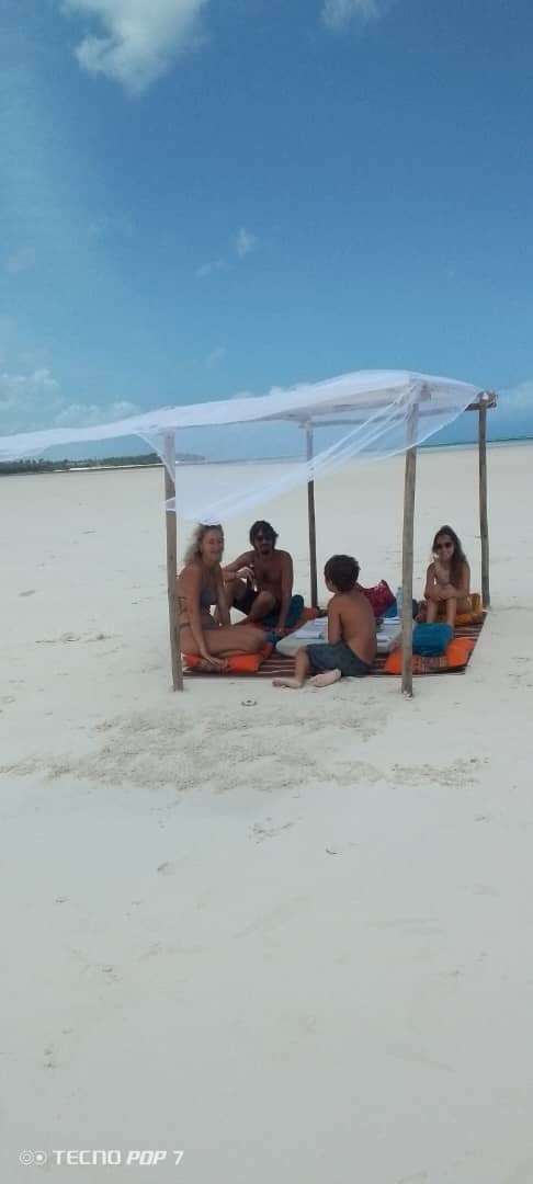Guests sitting on cushions under a makuti shade on a white sandbank