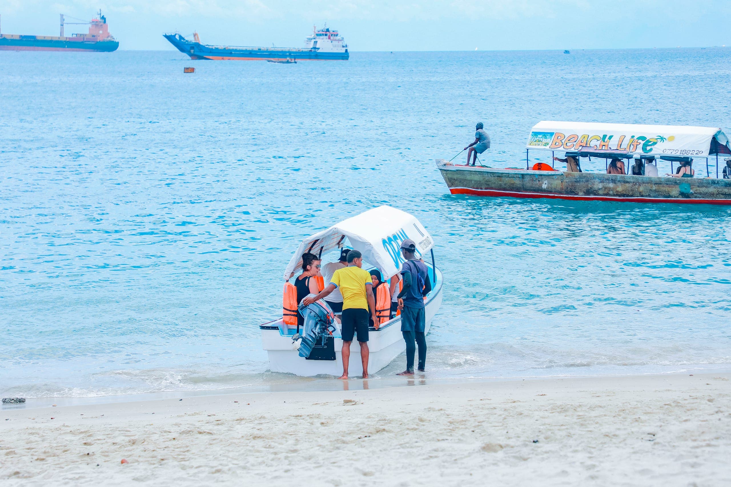 Guests in life jackets climbing aboard a small covered boat from the Stone Town beach