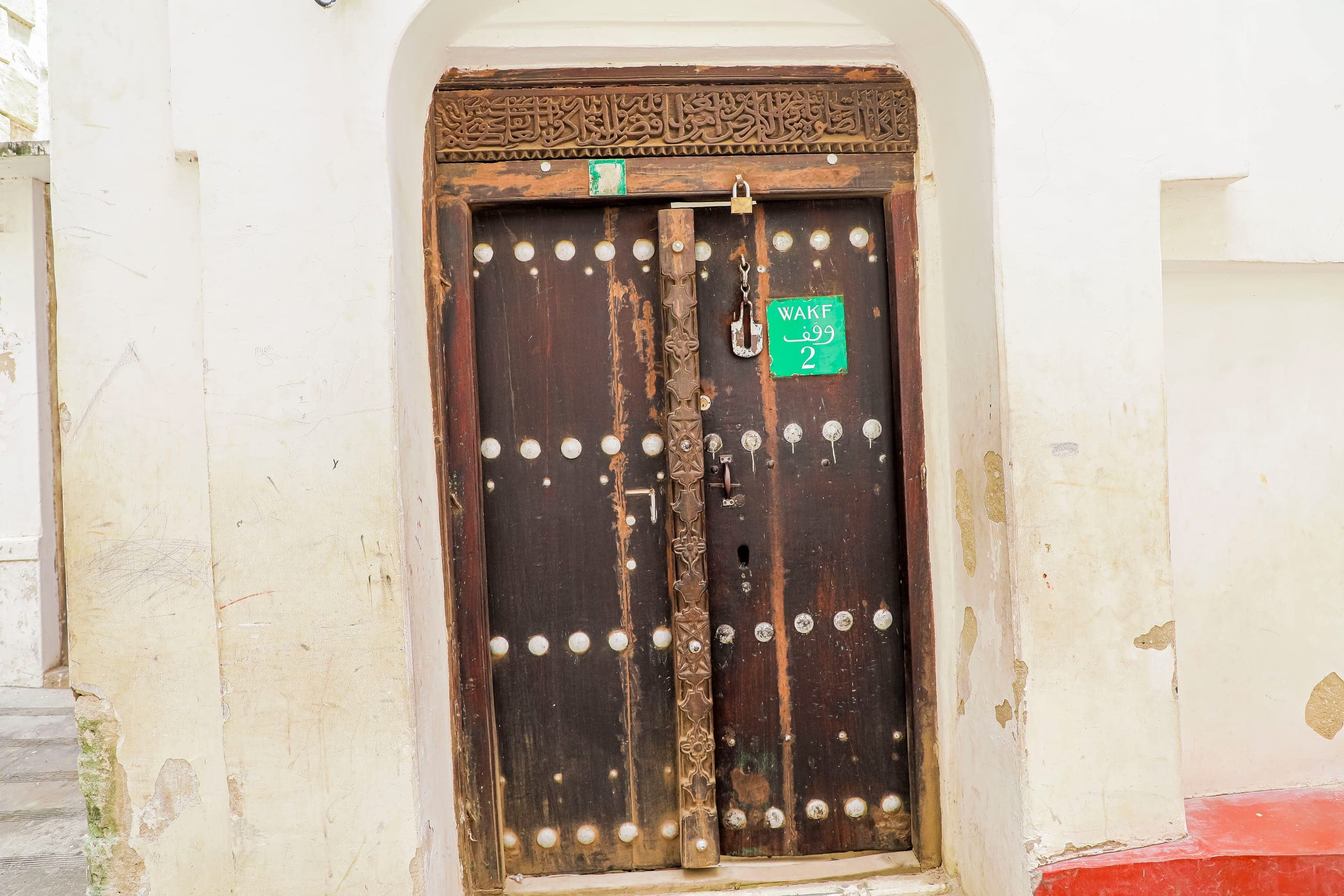 A carved wooden Stone Town door studded with brass, set in a whitewashed coral stone wall
