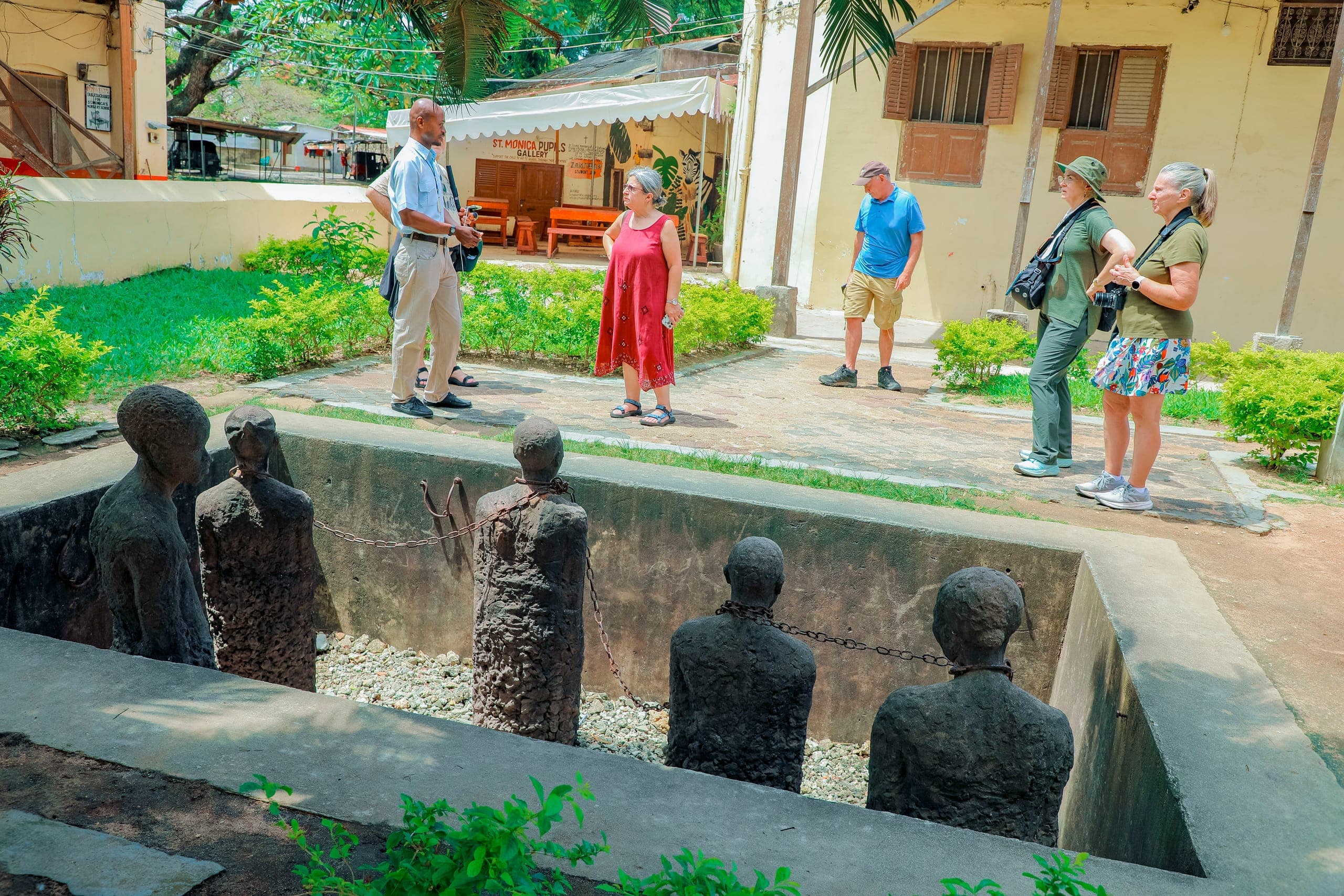 Guests with a Tima Tours guide above the chained figures of the slave market memorial in Stone Town