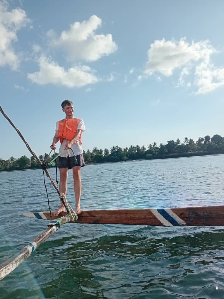 A guest in a life jacket standing on the outrigger of a wooden dhow off Zanzibar