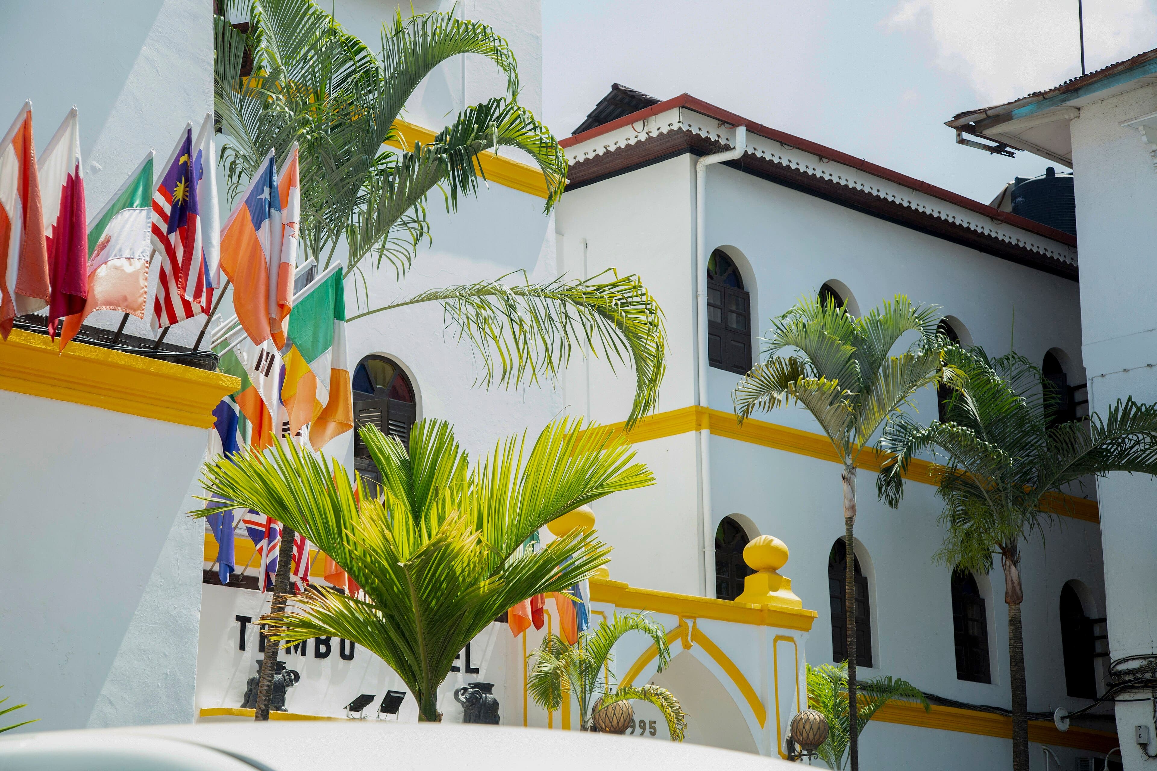 The white front of Tembo House Hotel on the Stone Town seafront, with palms and a row of flags