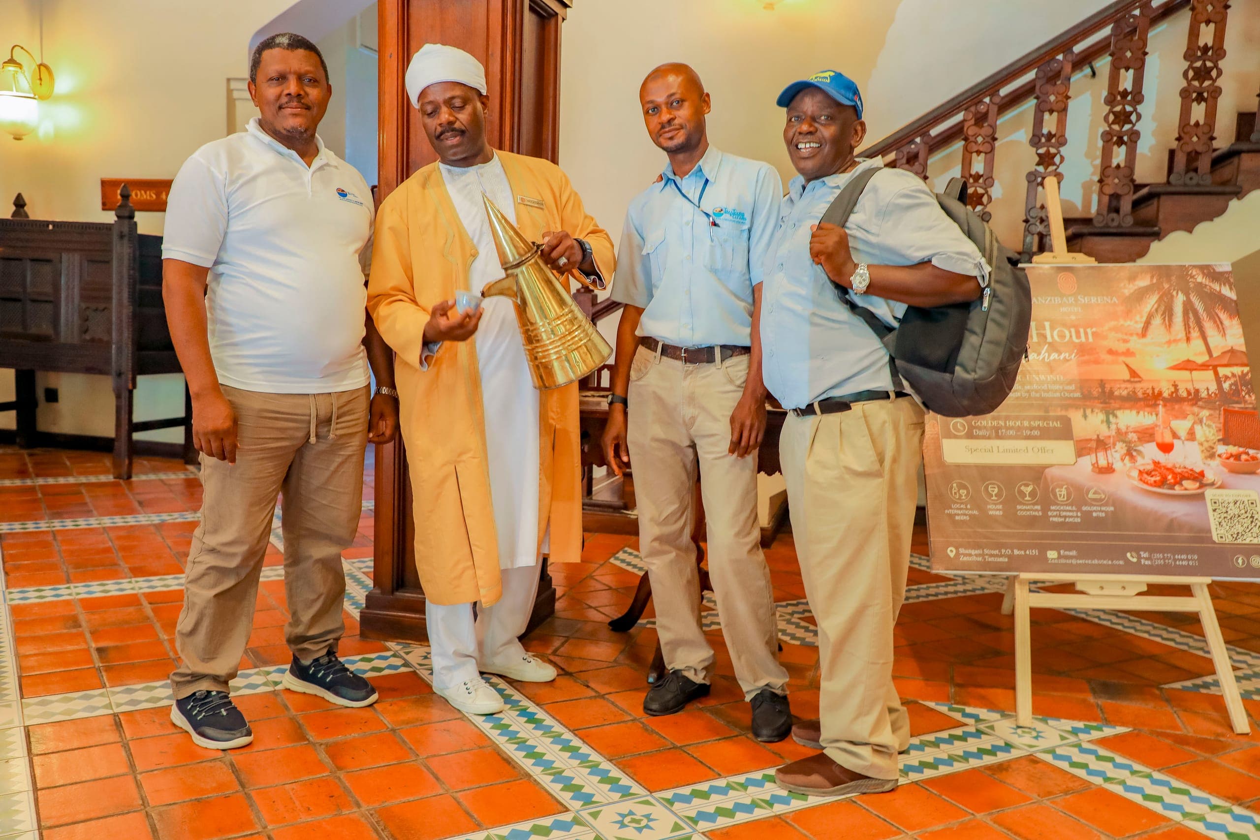 Salum and two Tima Tours guides in uniform standing with a coffee seller in a yellow kanzu in a Stone Town hotel hall